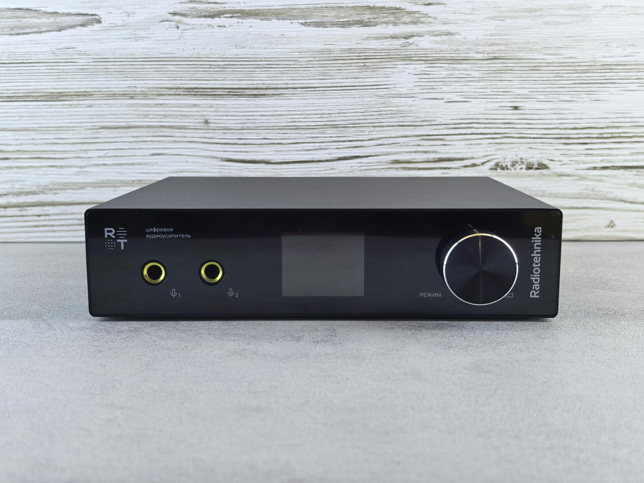 Black audio amplifier with minimalist design and yellow inputs on a wood-patterned backdrop.